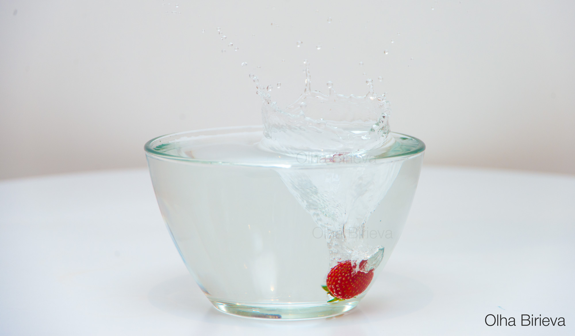 A single fresh strawberry is dropped into water